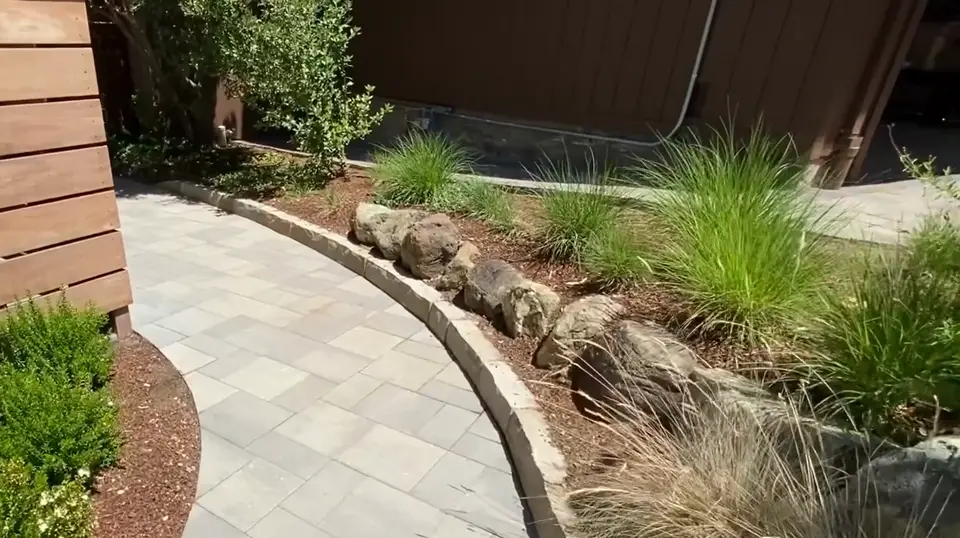 Curved paver path with a boulder edge through a garden