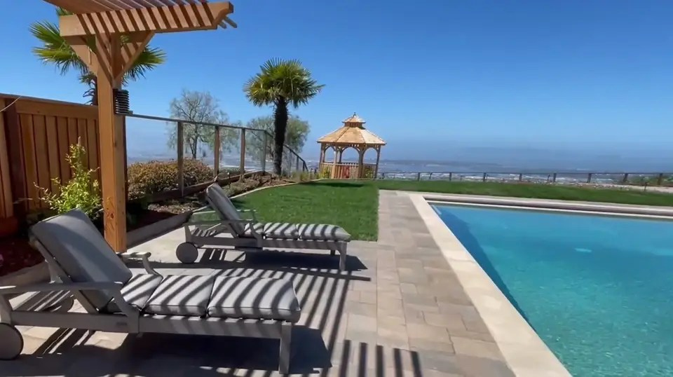 Pool deck with lounge chairs, turf lawn and view beyond the fence